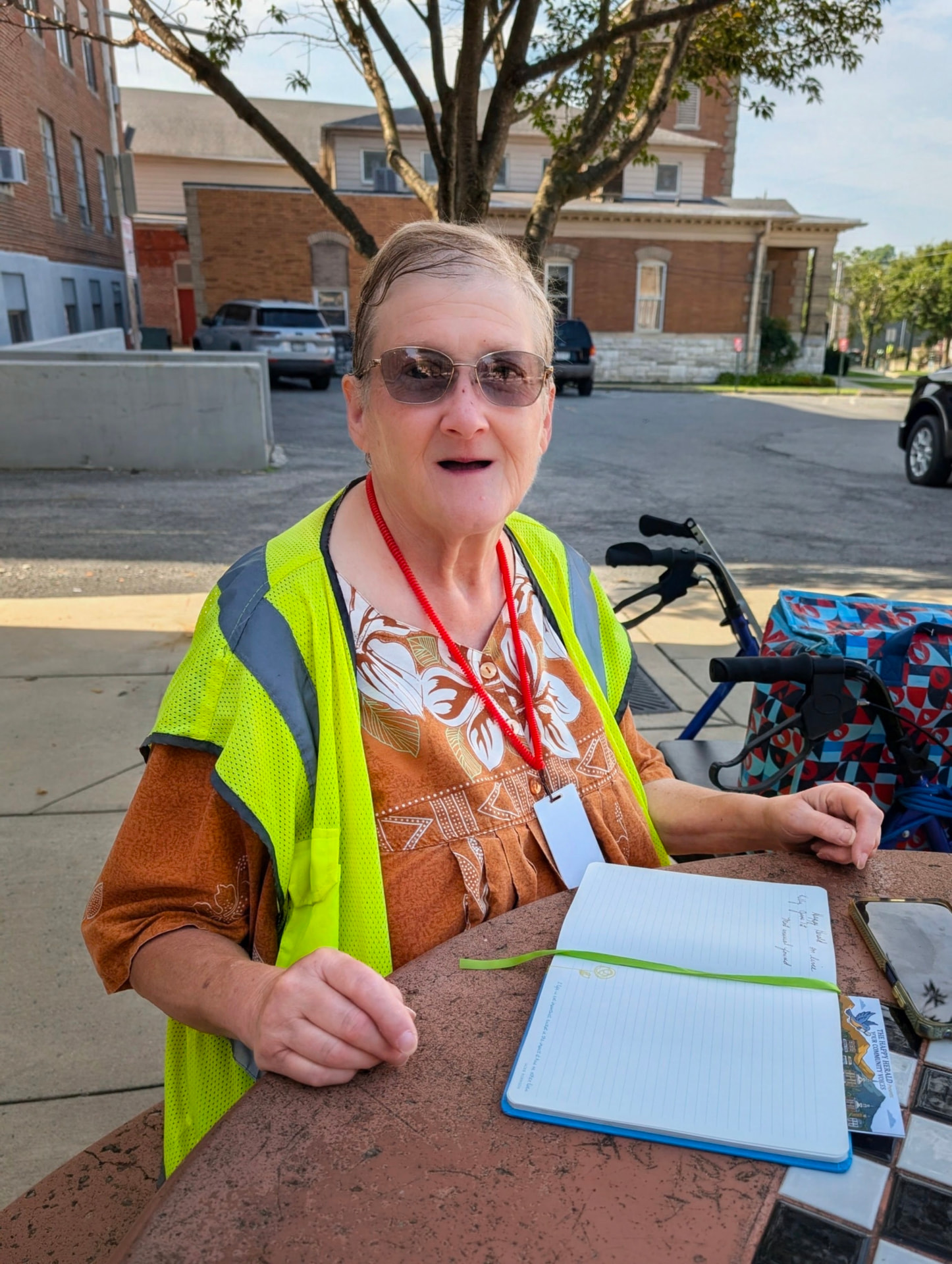 Miss Mary Mullin in a bright safety vest, seated at a downtown Martinsburg table with her notebook.